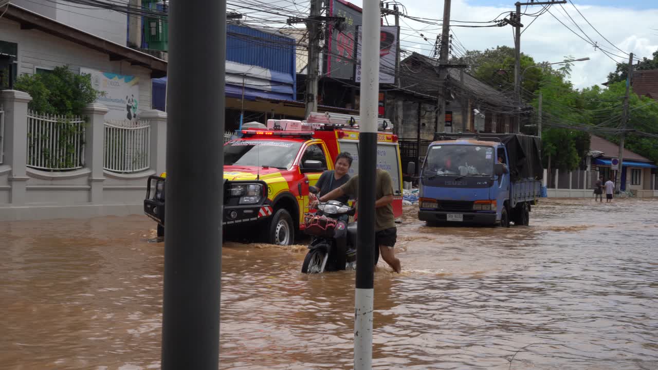 A fire and rescue truck is seen as two individuals walk alongside it through a street completely flooded water above their knees severe flooding in Chiang Mai-Lamphun Road, Wat Ket, September 2024
