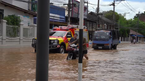 a fire and rescue truck is seen as two individuals walk alongside it through a street completely flooded water above their knees severe flooding in chiang mai-lamphun road, wat ket, september 2024