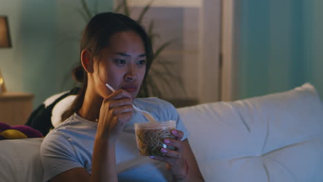 woman eating noodles on the sofa at night