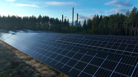 Vista-Aérea-Sobre-Un-Campo-Solar-Con-Fondo-De-Planta-De-Energía,-Día-Soleado-De-Otoño