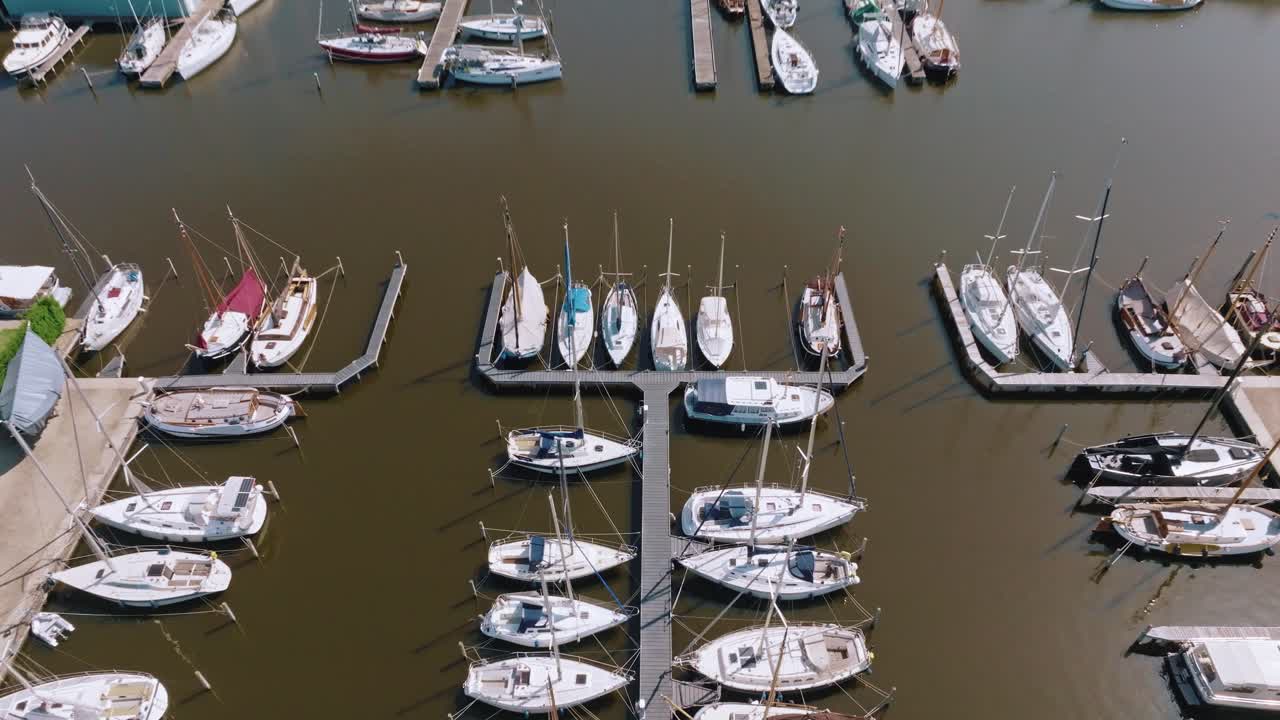 Drone rising in place reveals multiple docked boats and marina buildings under morning sun