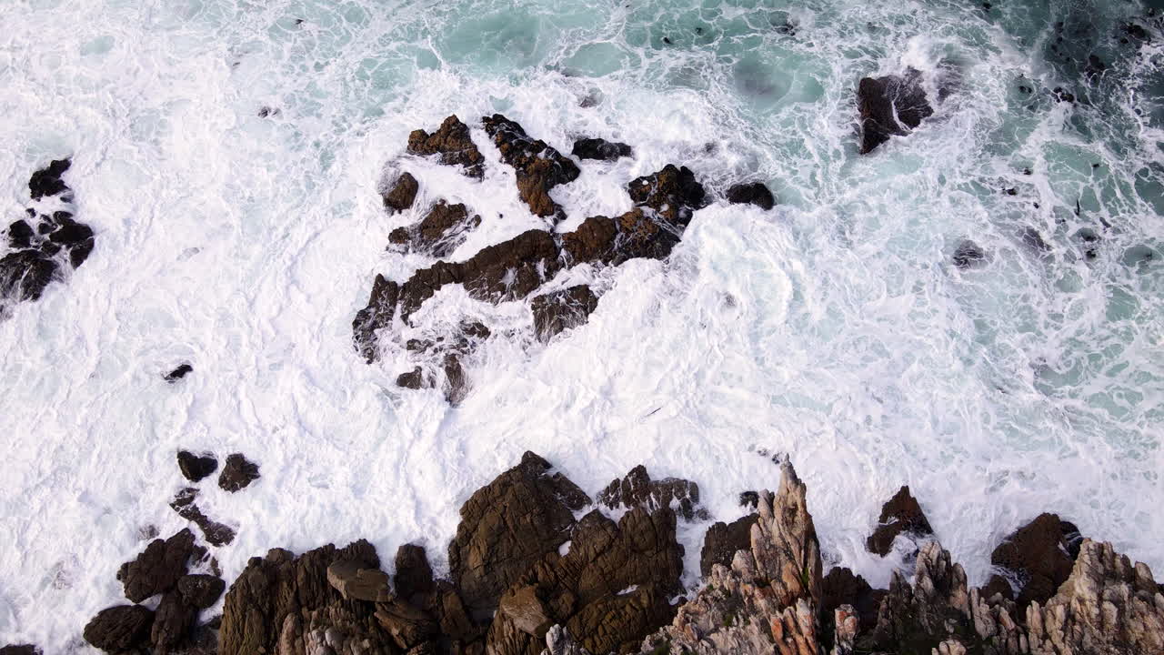 Frothing white seawater waves crash into rocky Atlantic coastline, aerial slomo