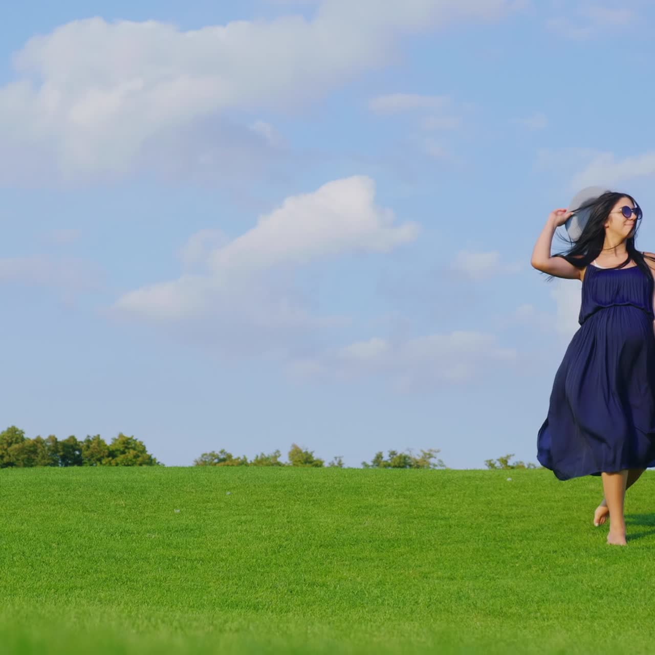 una mujer embarazada con un vestido ligero camina despreocupada por un prado verde 1