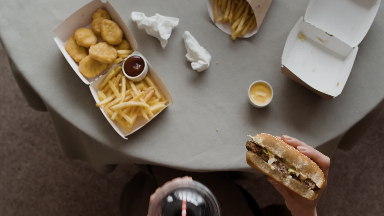 Overhead view of a person enjoying a fast food meal with chicken nuggets, fries, burger, and soda