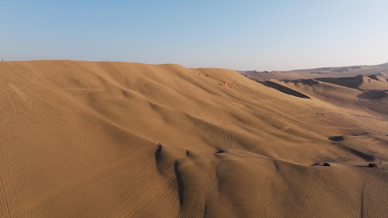 Aerial sweep glides over tall dunes showing rhythmic sand ridges stretching across the desert basin, dolly establishing