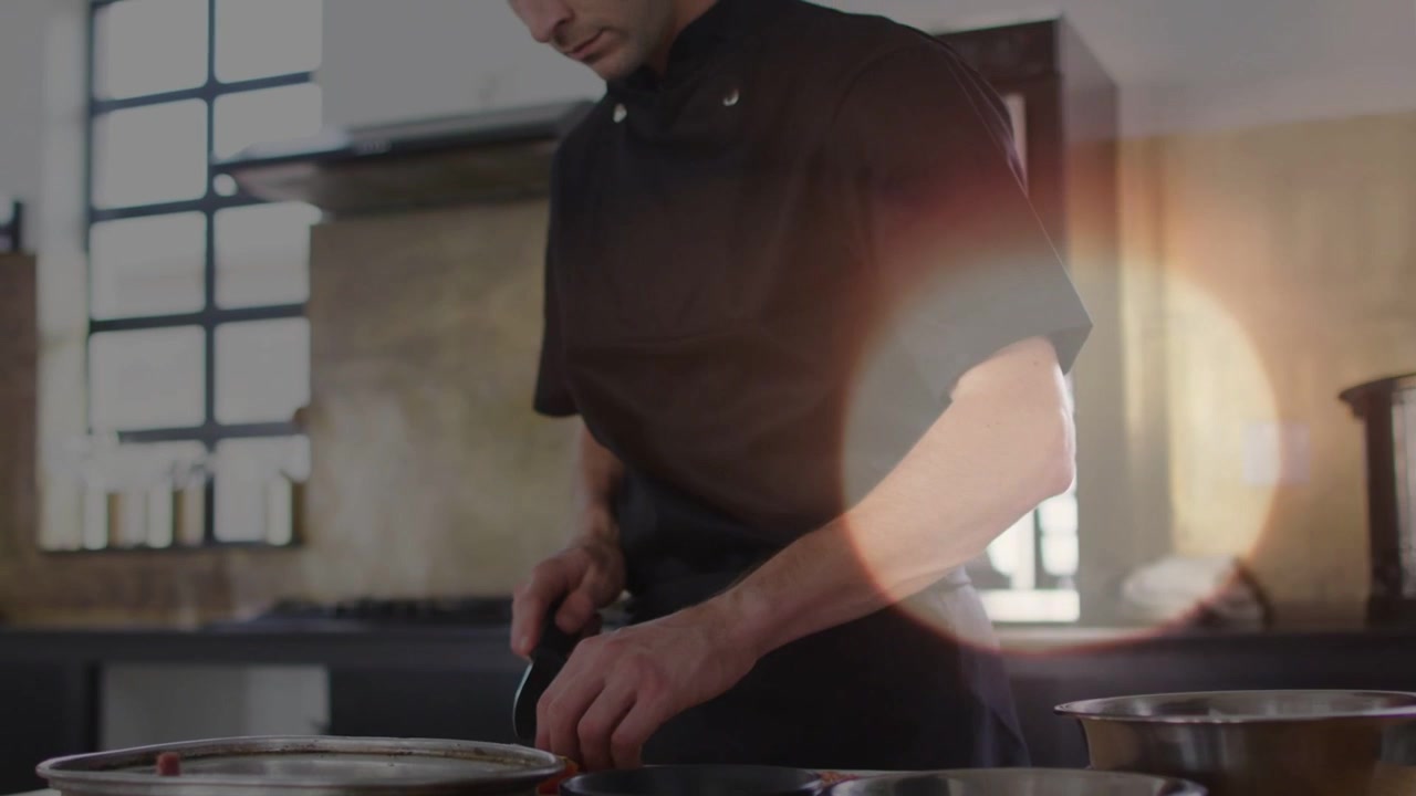Ripresa all'indietro che mostra uno chef che taglia con un coltello, mentre sistema ciotole per la preparazione in cucina, con bagliori dell'obiettivo che fluttuano.