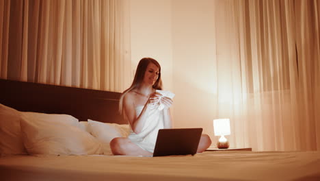 mujer relajándose en la cama con una computadora portátil y café