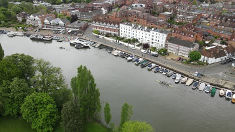Henley-on-Thames-waterfront-boats-moored-and-rowers-moving-along-rive-Oxfordshire-UK-Aerial-footage