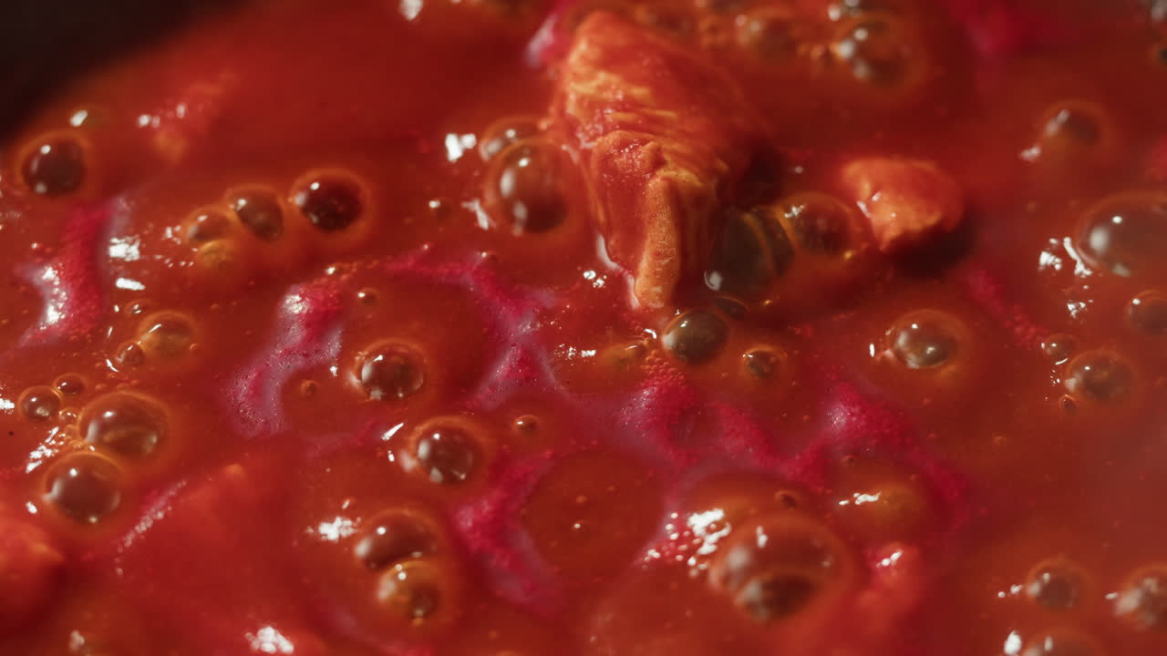 Chicken in tomato sauce is boiling on a frying pan with spices. Cooking tomato sauce curry with chicken fillet. Traditional Italian Mexican Asian dish. High quality studio shot for cafe, restaurant close up.