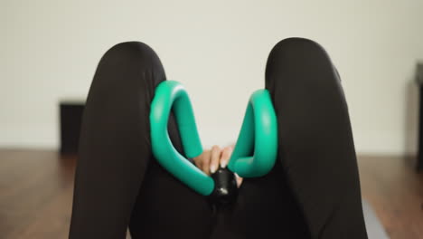 lady works out using thigh strengthener closeup. active woman employs leg muscle exerciser lying on floor in personal workout space. body strength