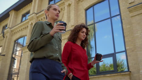 young female professionals walking in city with paper cups