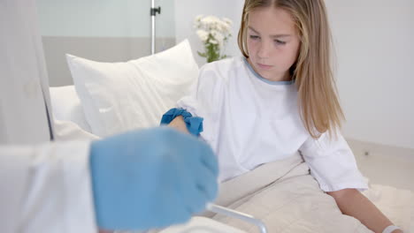 diverse male doctor taking blood sample from girl patient in bed with syringe, slow motion