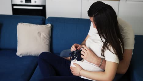 lovely pregnant woman and her husband holding baby shoes on belly