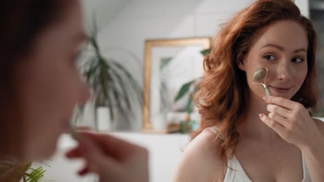 Smiling-caucasian-woman-using-face-roller-in-the-bathroom.