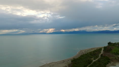 ariel drone disparado volando desde la costa a través de la bahía de tasmania con montañas en el horizonte durante la puesta de sol, nueva zelanda