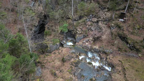 Flowing-water-cascades-between-large-boulders-in-meadow-clearing-of-leafless-trees