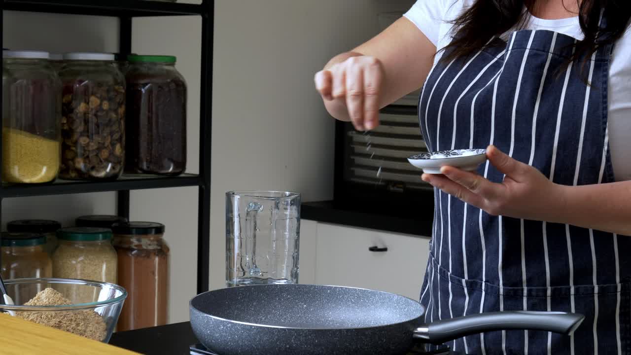Female chef sprinkles pinches of salt into a pan on top of a stove