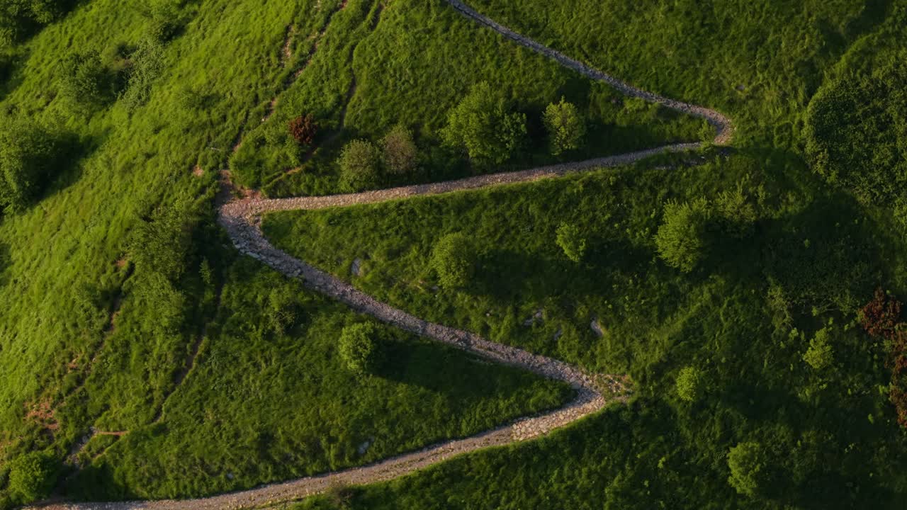 Winding stone paths lead through green grass and trees near an ancient Italian fort