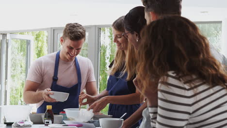 female teacher with male student mixing ingredients for recipe in cookery class in kitchen