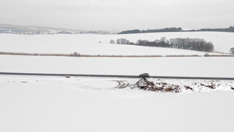 Tracking-Aerial-Shot-Of-A-Car-Driving-In-A-Rural-Winter-Landscape-With-Fresh-Snow