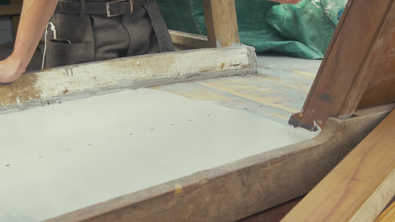 joven carpintero pintando la cubierta de teca de un viejo barco de madera con un primer protector a base de aluminio