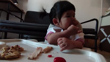 linda niña asiática comiendo su comida casera en una silla de alimentación para bebés