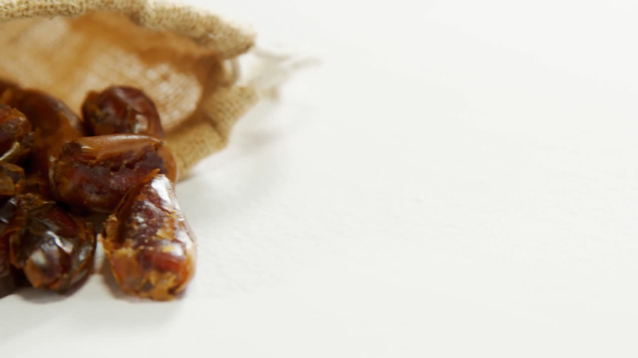 Dates spilling out of sack on white surface 4K 4k