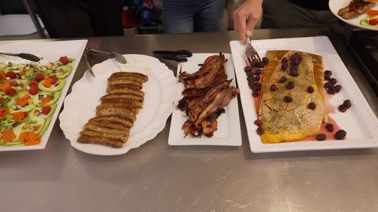 Folk står i kø ved en buffet og tager mad fra et udvalg af salat, fisk og pølser. En travl scene med selvbetjening i en restaurant eller på et hotel, der viser variation, gæstfrihed og menneskemylder.