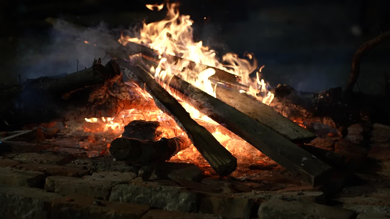 Holzfeuer, das nachts im Dunkeln mit roten Flammen und warmen Funken brennt