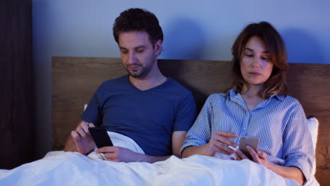 couple caucasien assis sur le lit et utilisant des smartphones, puis ils disent bonne nuit à leurs fils