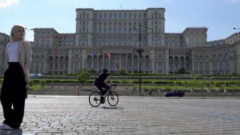 Elegant-Woman-In-A-White-T-Shirt-Walking-Towards-The-Camera-And-Enjoying-The-View,-Palace-of-the-Parliament-In-The-Background,-Bucharest,-Romania