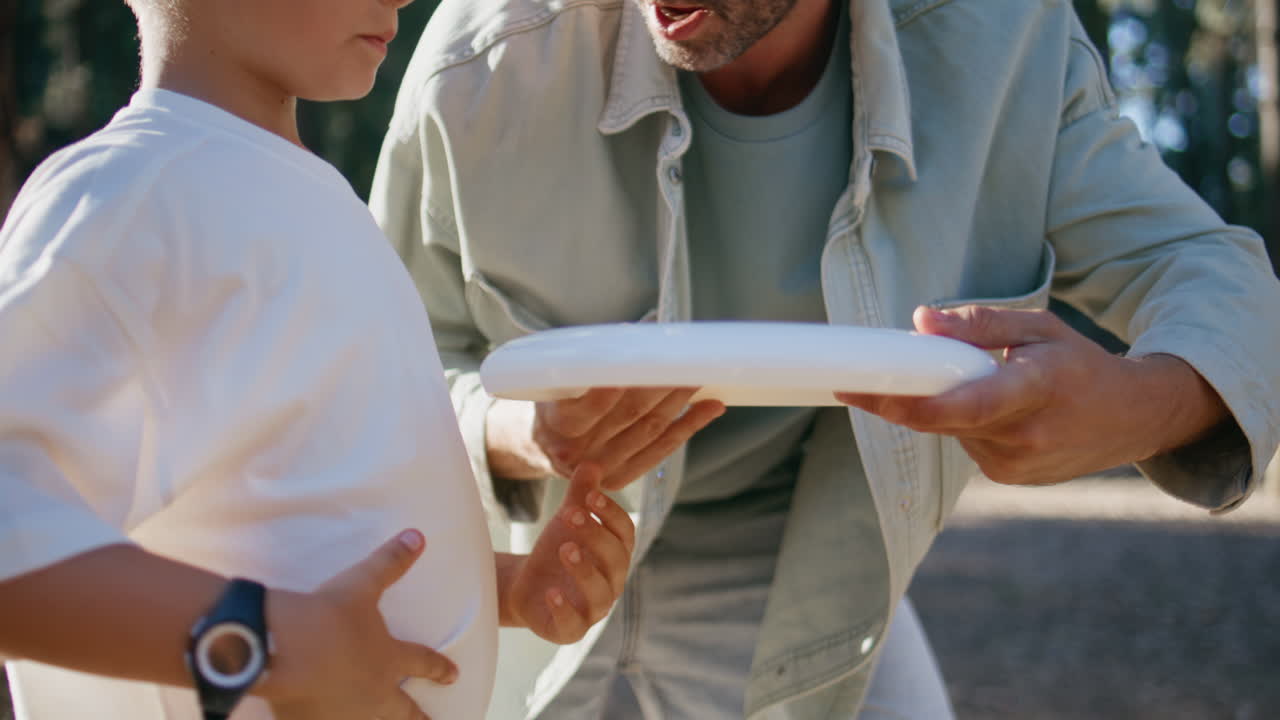 Father teaching son frisbee game in sunbeams park closeup. Man talking to boy