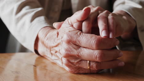 close-up of elderly hands with wrinkles and a ring on a wooden table