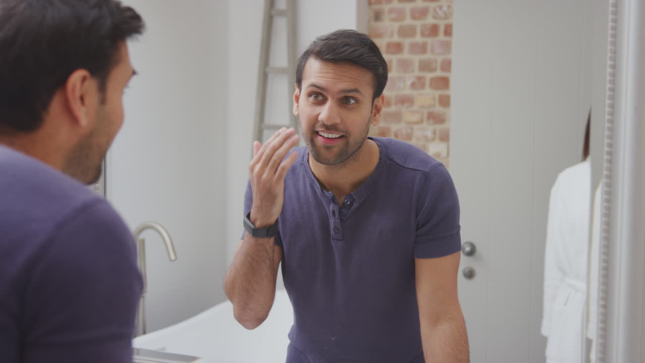 목욕복과 피자마를 입은 부부는 집에서 목욕실 거울에 준비하고 있습니다.