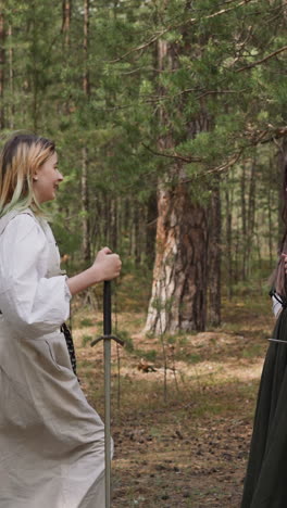 girls teenagers in long vintage medieval dresses hold long swords in forest slow motion. camp of historic events reconstruction. hobby and leisure