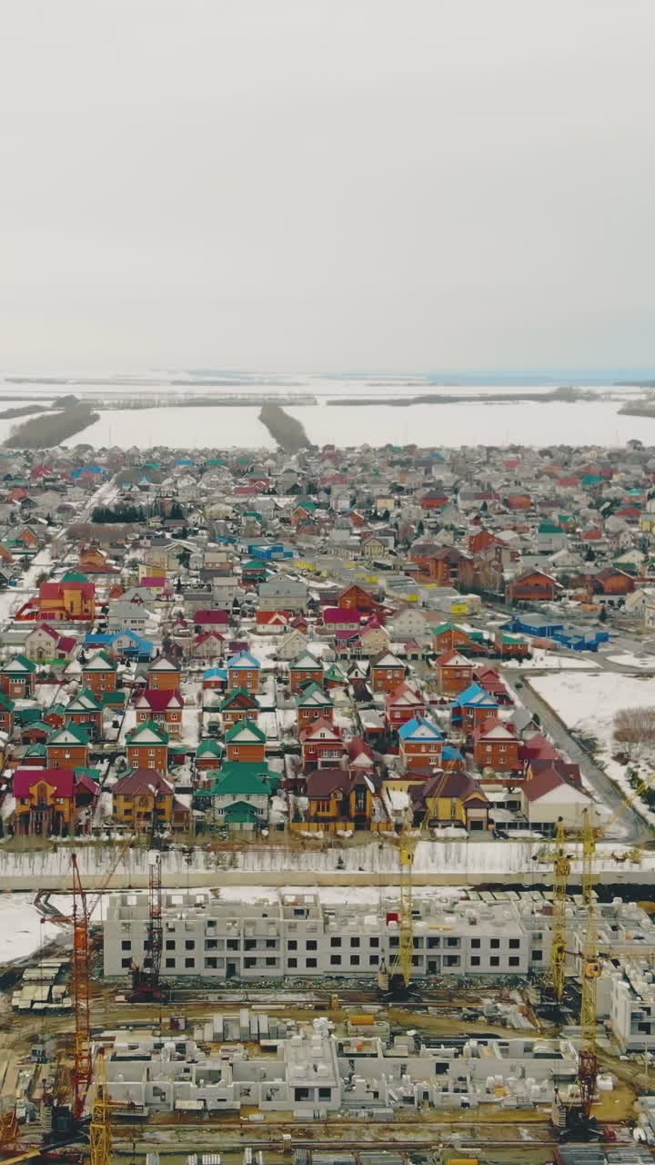 light gray building ongoing project with yellow construction cranes against residential cottage town bird eye view