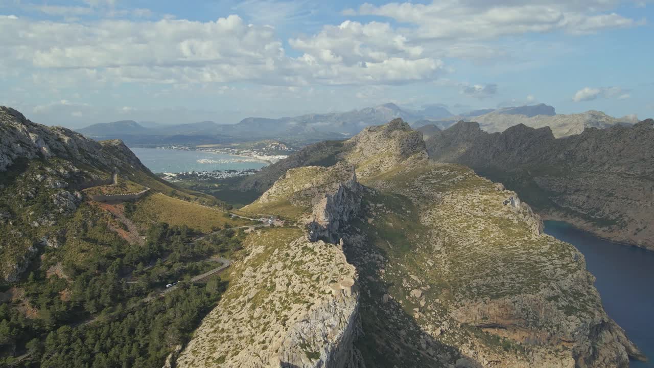 A dramatic aerial view of a rocky mountain ridge with a winding stone path leading to a panoramic viewpoint in Mallorca, Spain.