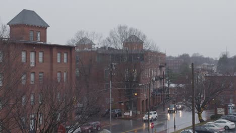 a wide shot of traffic moving through an intersection of a sleepy town while rain pours down