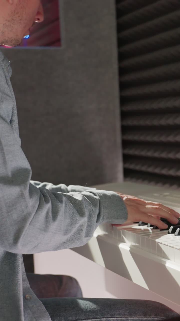 A focused man in a long sleeve shirt sits at a white piano in a studio with a black background, reflecting a mix of creativity and professionalism. The scene is lit to enhance the artistic atmosphere
