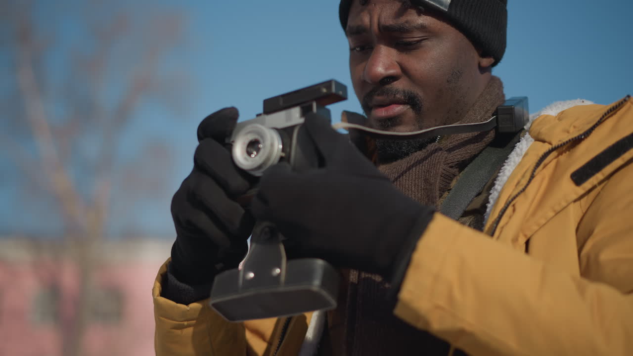 photographer with camera hanging on neck holding camera out and looking around both sides while walking along snow covered urban walkway under crisp blue winter sky