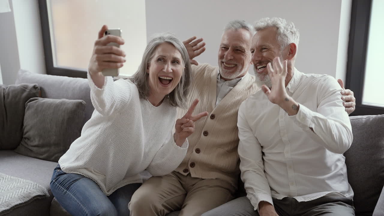 grupo de felices amigos mayores sentados en el sofá y tomando un video selfie