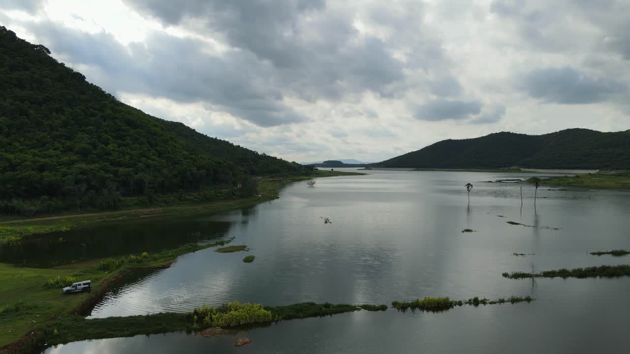 Aerial footage sliding towards the left revealing the beautiful lake and mountains then a truck and some people getting ready to leave after fishing for the whole day; Saraburi, Thailand