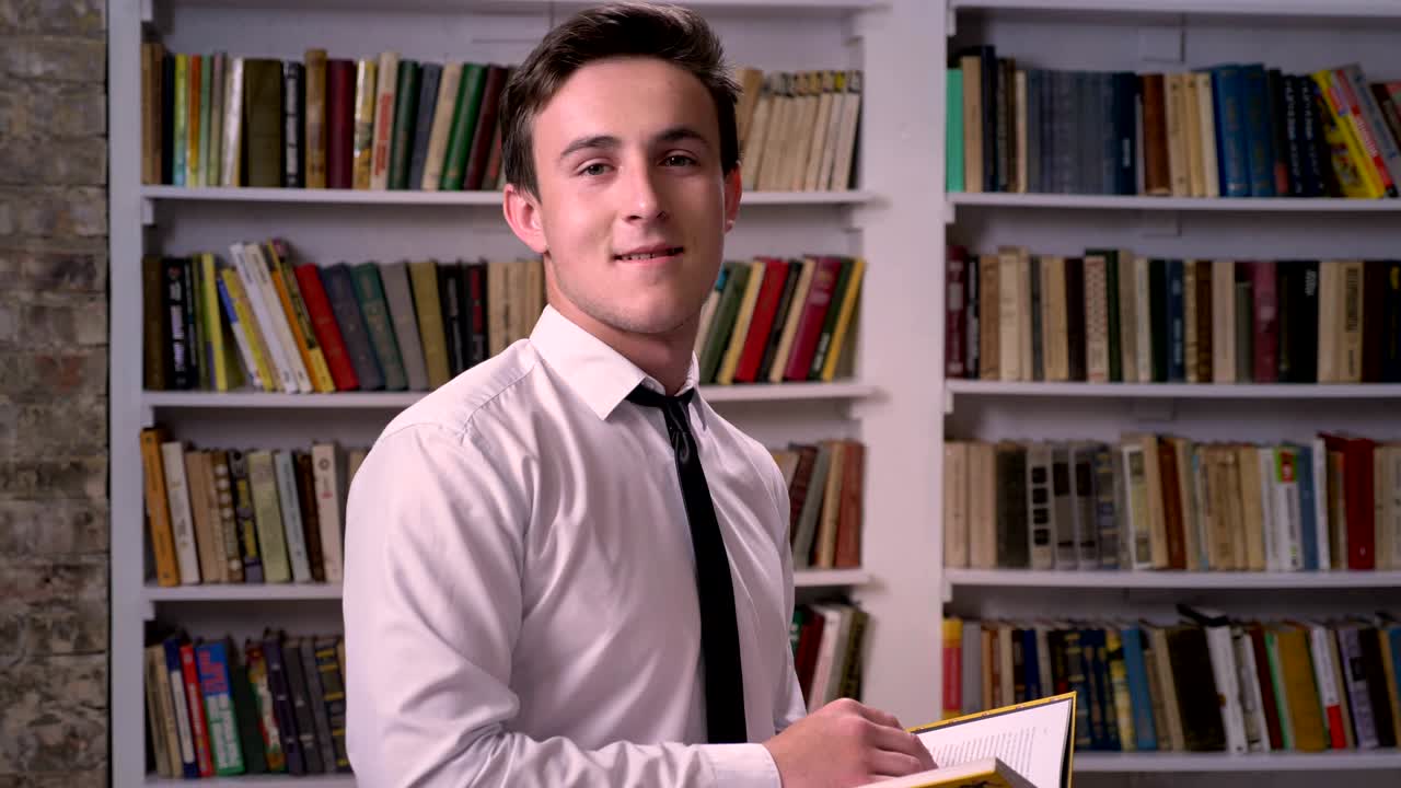 Young businessman is reading book in library, watching at camera, relax concept