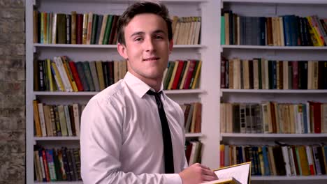 young businessman is reading book in library, watching at camera, relax concept