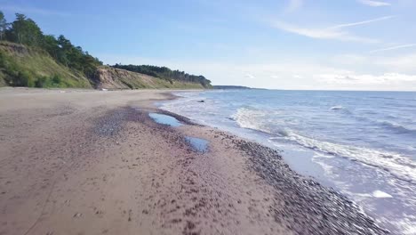 aerial view of baltic sea beach at jurkalne on a sunny day, white sand cliff damaged by waves, coastal erosion, climate changes, wide angle drone shot moving backward low
