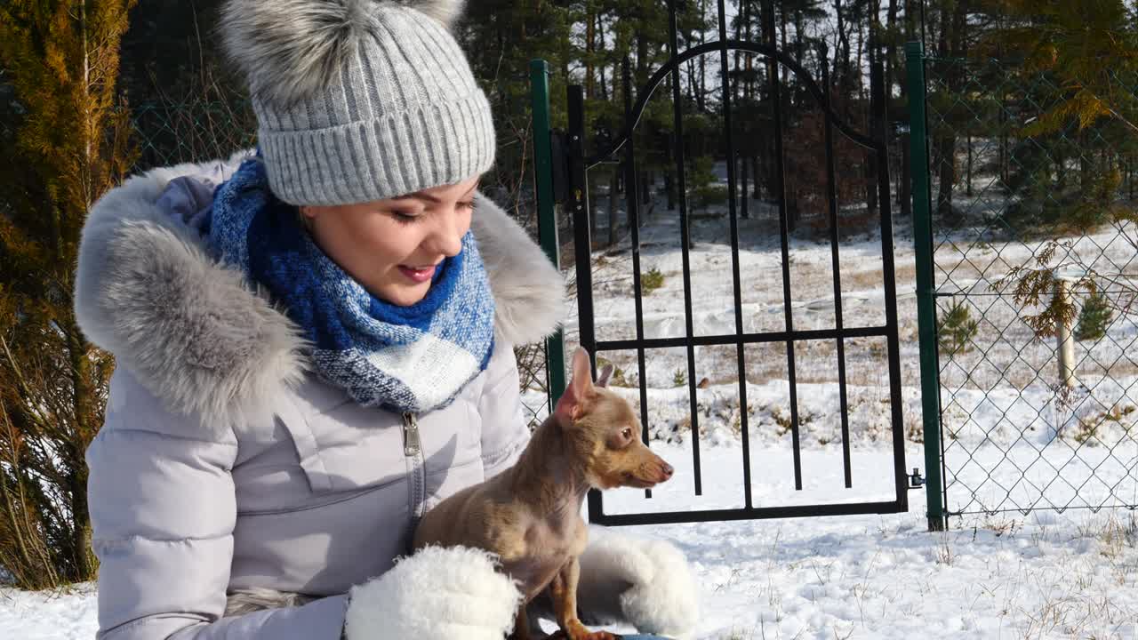 여자 는 겨울 밖 에서 작은 개 와 함께 놀고 있다