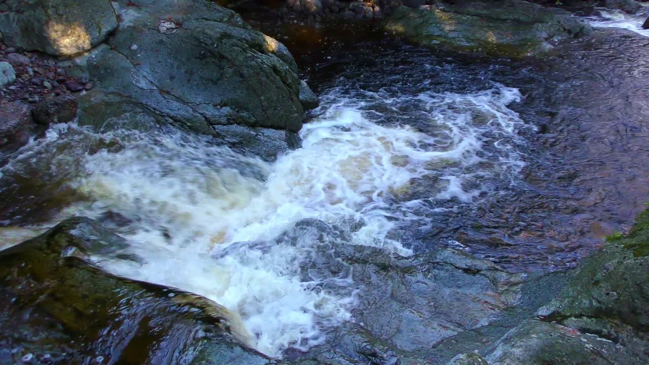 Cascata di torrente di montagna sulle rocce, sotto una luce screziata in una fredda giornata invernale