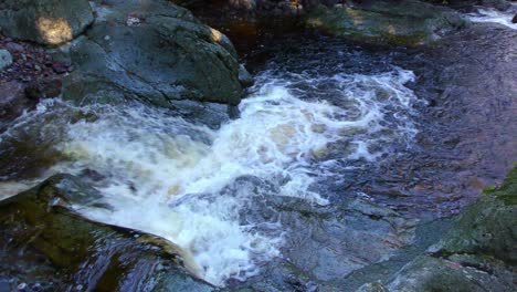 Mountain-stream-cascade-over-rocks-in-dappled-light-on-a-cold-winter-day