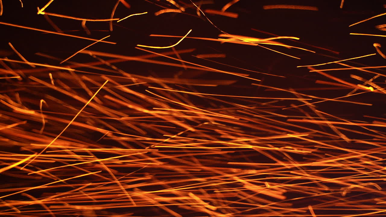Red hot sparkles of fire flying horizontally at a very fast speed. Orange particles isolated on the black background.