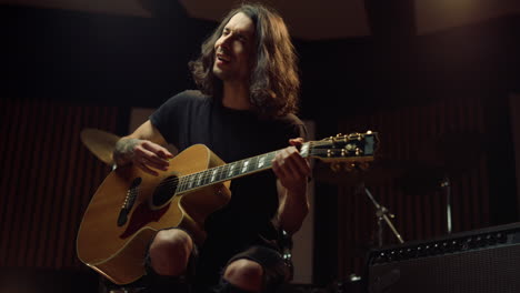 hombre alegre tocando la guitarra acústica en el estudio de música